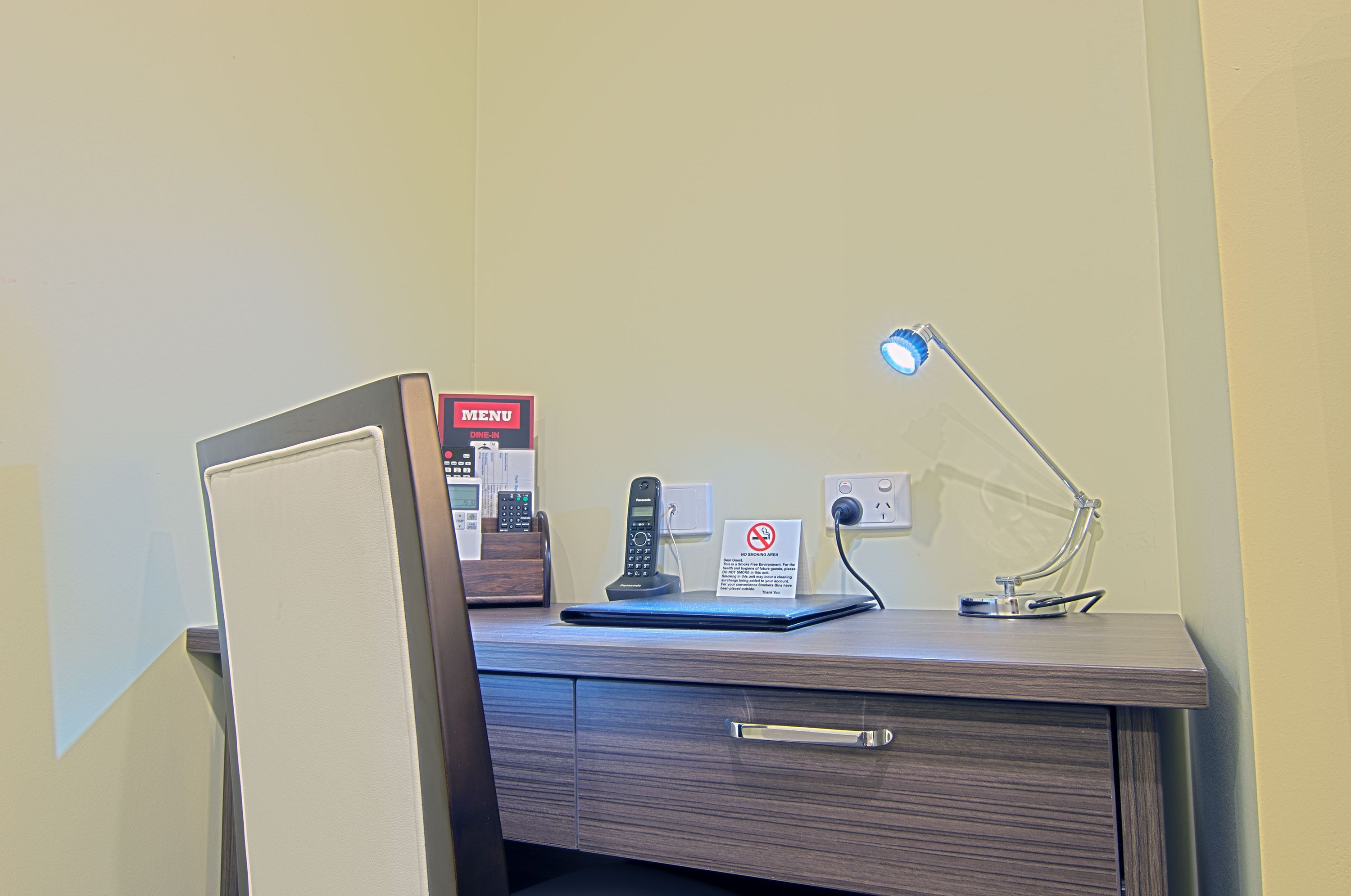 A desk with a phone, a menu sign, a no-smoking sign, and a desk lamp.