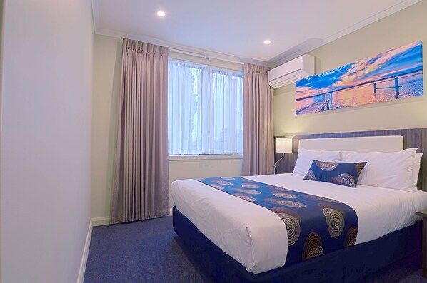 A hotel room with a large bed, a window with curtains, a painting on the wall, and an air conditioning unit. - Park Squire Motor Inn and Serviced Apartments (Parkville)