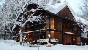 Ein großes, hölzernes Chalet mit mehreren Stockwerken, umgeben von schneebedeckten Bäumen.