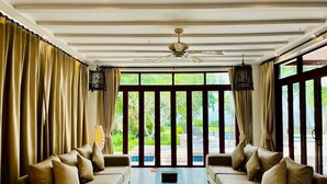 A spacious living area with two sofas facing a large window, a ceiling fan, and a view of a pool and greenery outside.