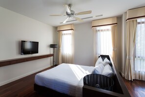 A hotel room with a bed, a ceiling fan, a flat-screen TV, and large windows with curtains. - Amatapura Beach Villa 12 (Krabi)