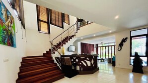 A spacious living area with a wooden staircase, a dining area, and large windows.