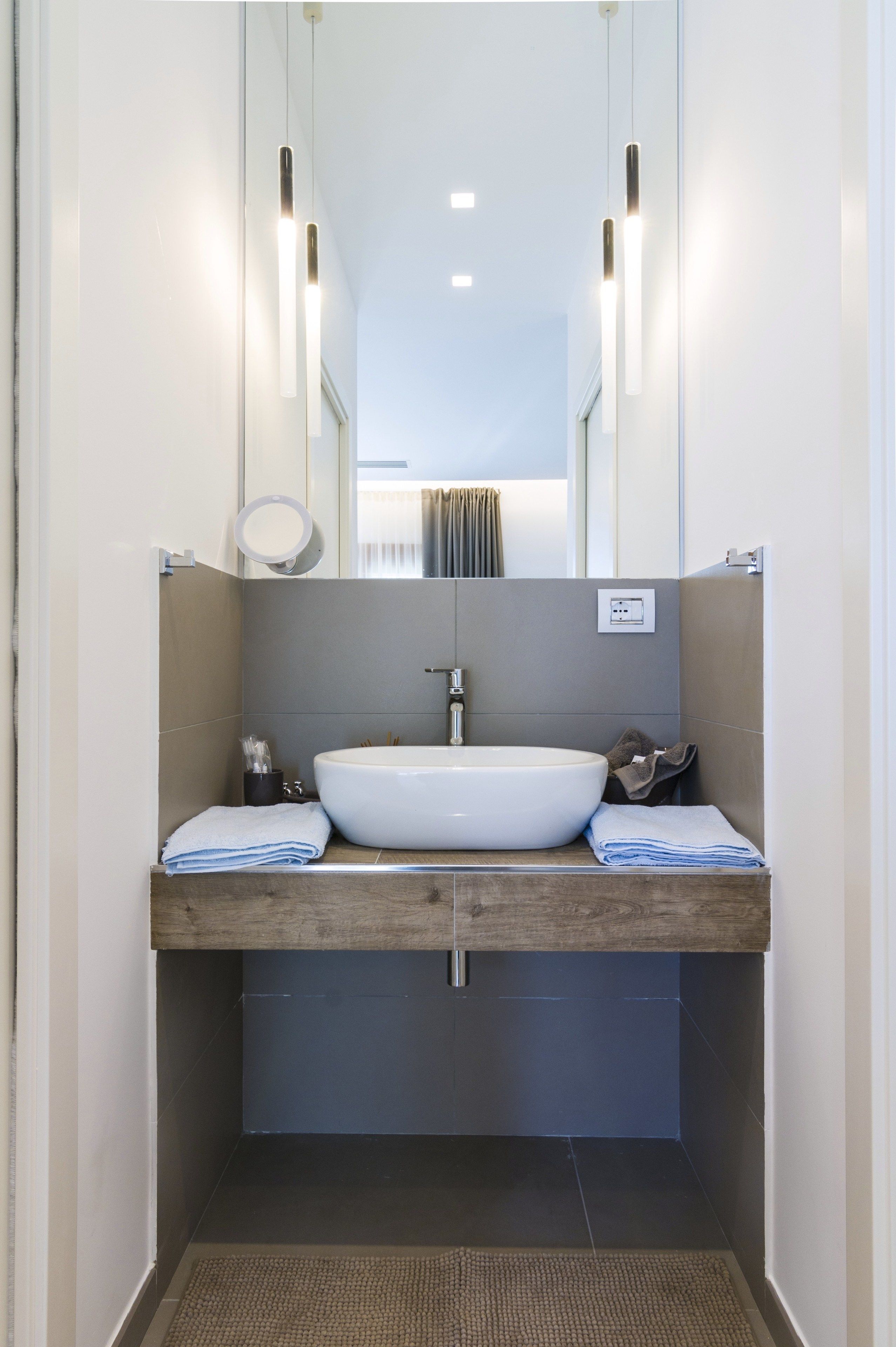 Un baño moderno con tocador de madera, un lavabo blanco y un espejo encima.