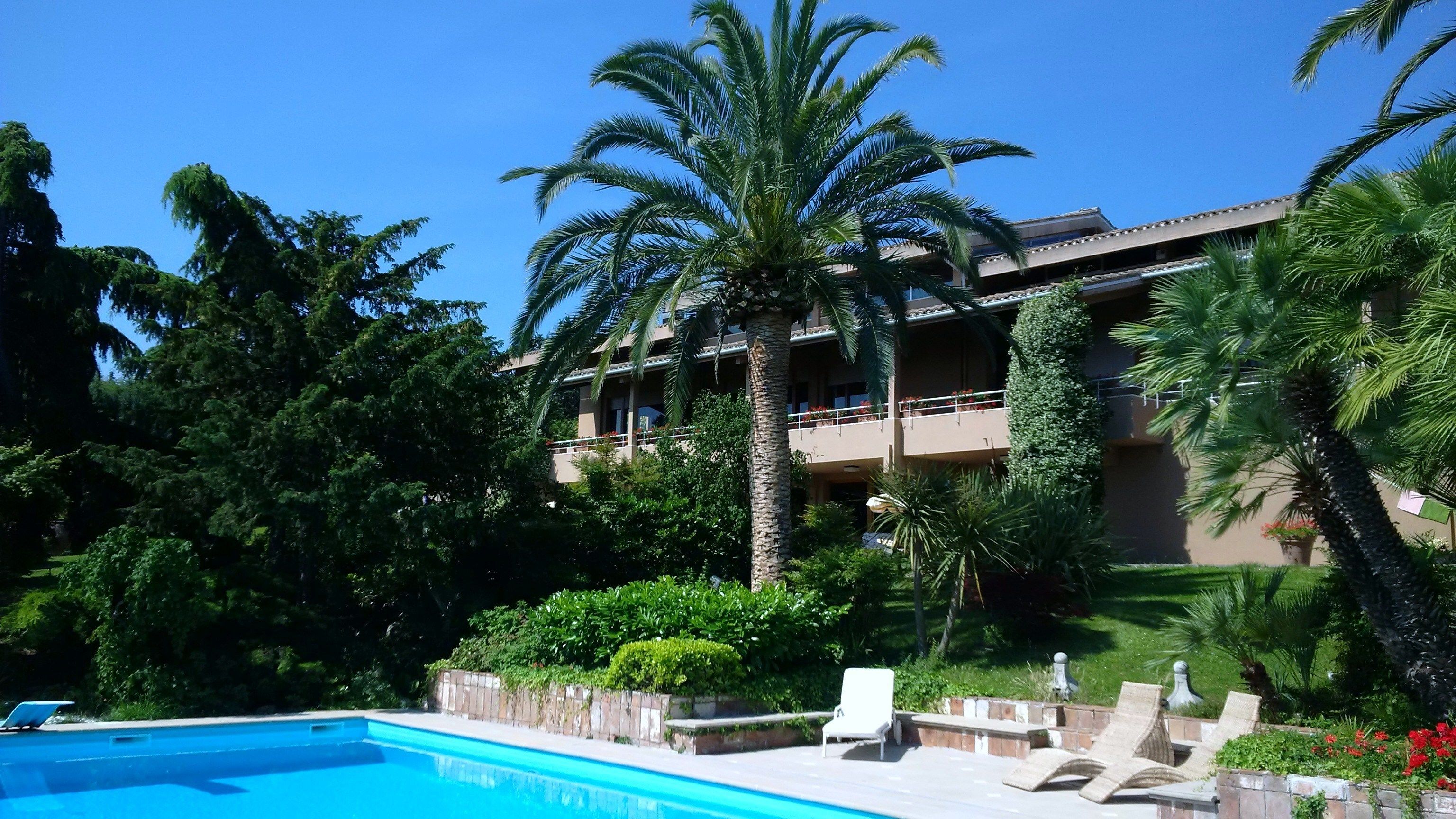 A hotel with a swimming pool, palm trees, and a multi-story building with balconies.