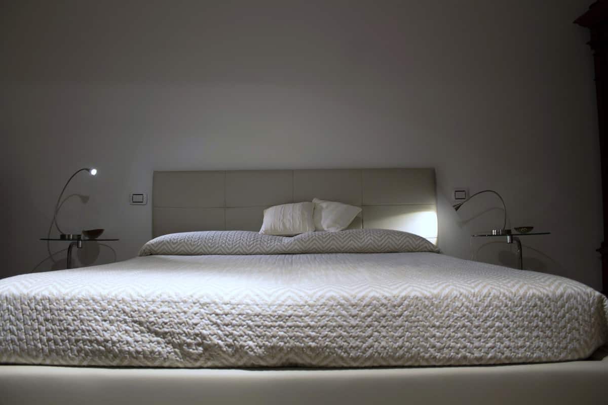 A large bed with a textured white duvet, two bedside tables with lamps, and a plain headboard.