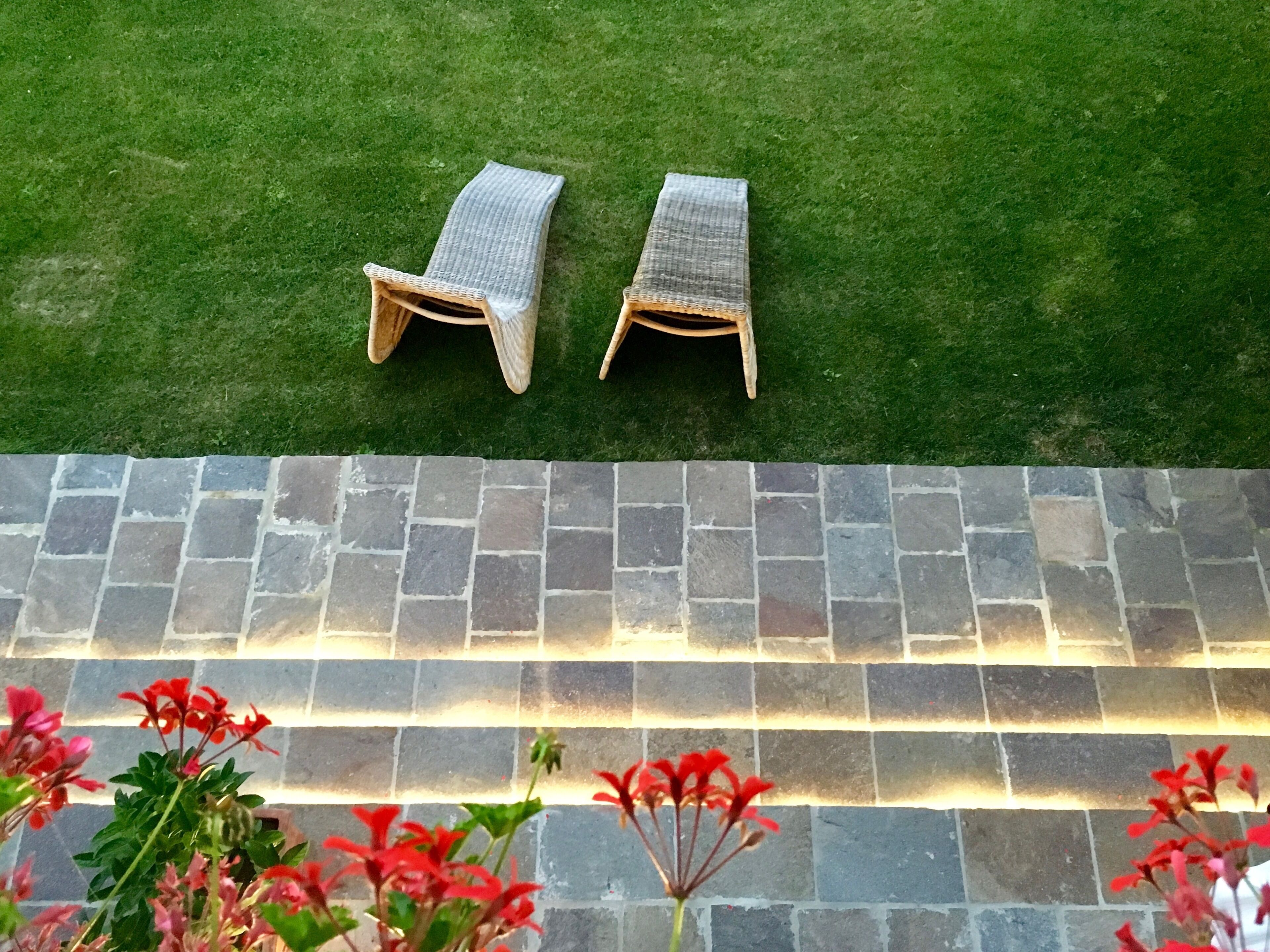 Two wicker lounge chairs on a green lawn, a stone pathway, and red flowers in the foreground.