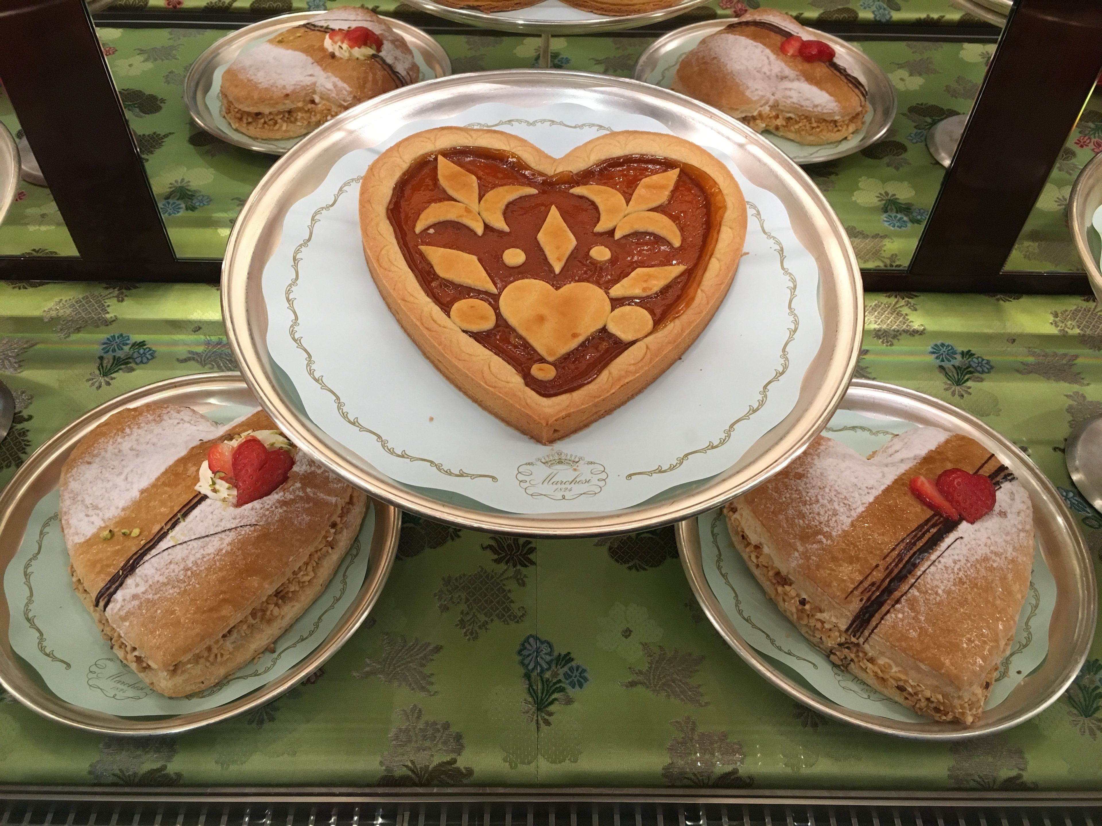 A dessert display with a heart-shaped tart at the center, surrounded by plates with pastries.