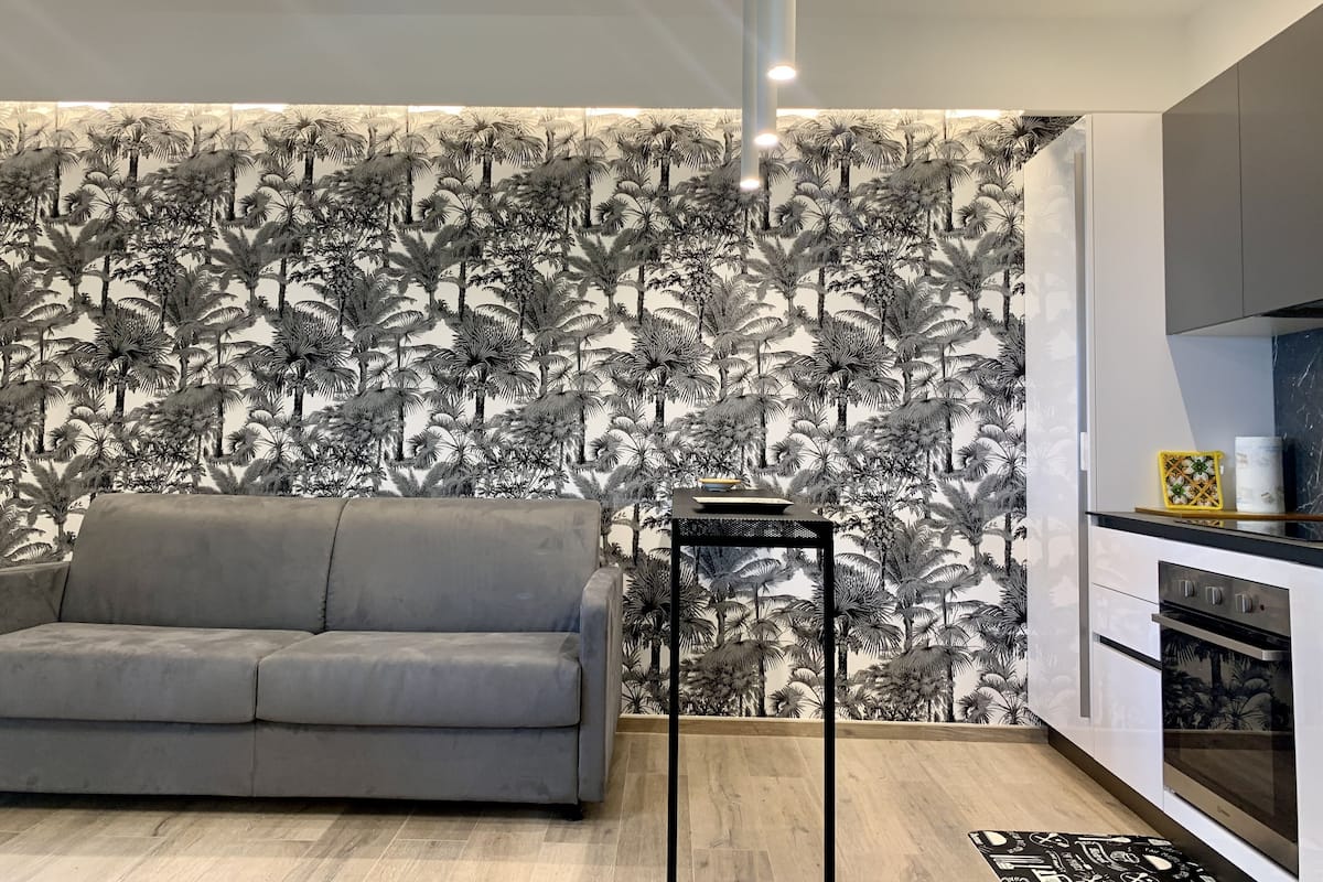 A modern kitchen with a grey sofa, a black side table, and a patterned wallpaper.