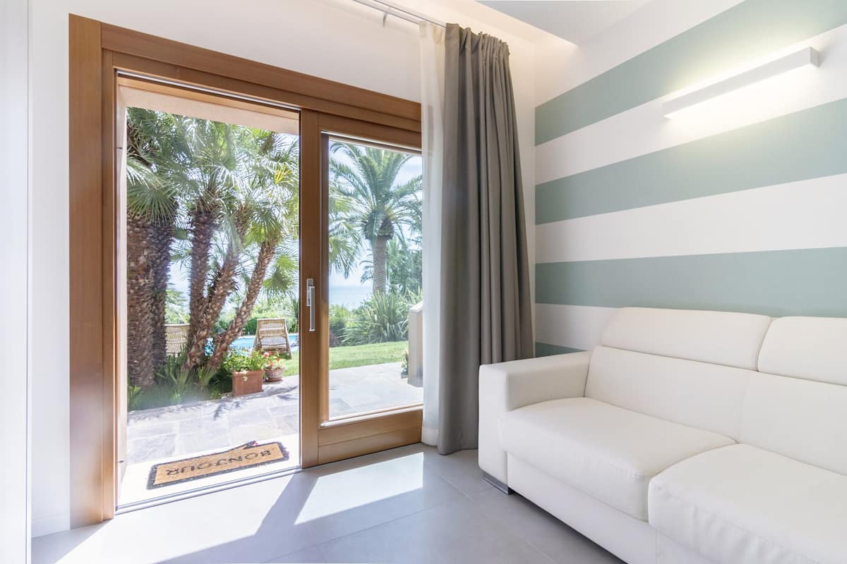 A room with a white sofa, a sliding glass door leading to a balcony with palm trees, and a striped wall.