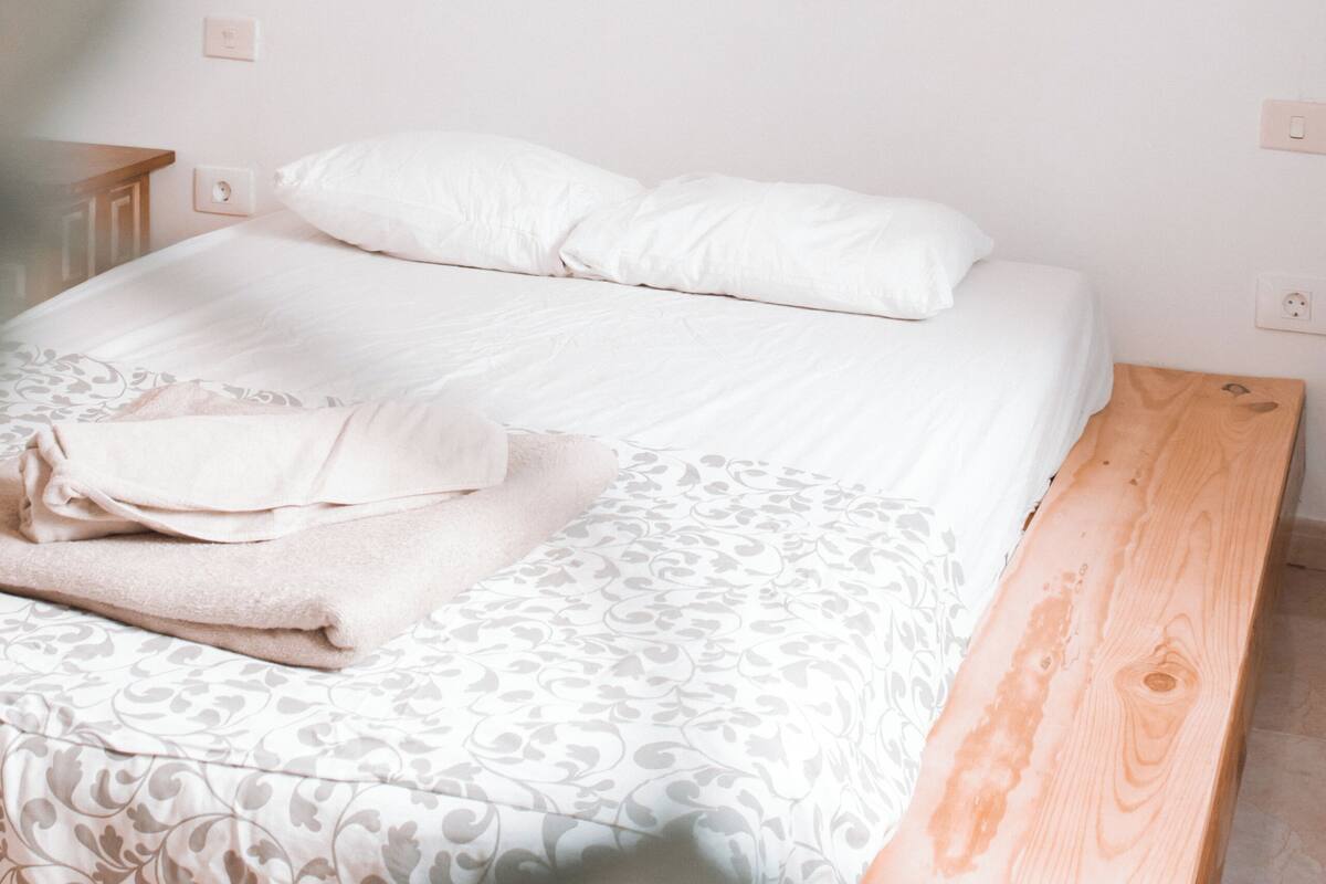 Un dormitorio con estructura de cama de madera, colcha estampada y lámpara fijada a la pared.