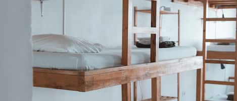 Bunk beds with wooden frames and white bedding, arranged in a dormitory-style room with white walls and tiled flooring.