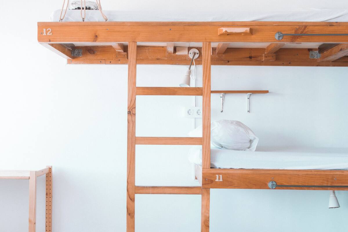 Una cama litera con escalera, pared blanca y estante de madera.
