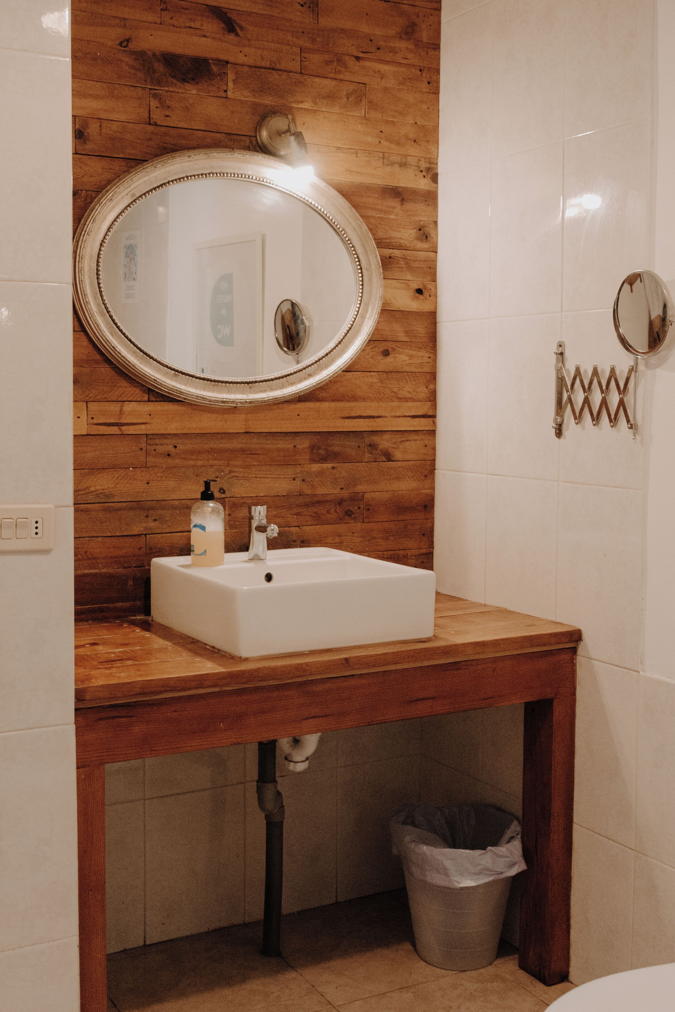 Une salle de bain avec un meuble-lavabo en bois, un lavabo blanc, un miroir et une poubelle.
