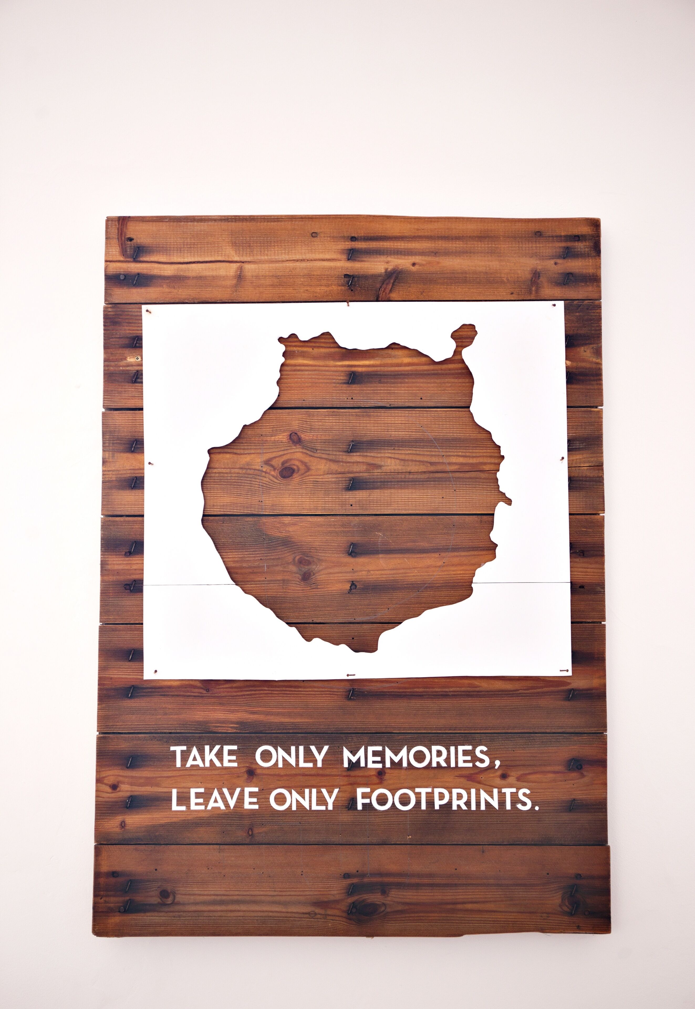 A wooden sign with a map outline and the text "TAKE ONLY MEMORIES, LEAVE ONLY FOOTPRINTS."