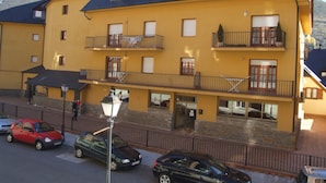 A multi-story building with balconies, a stone facade, and a parking area with cars.