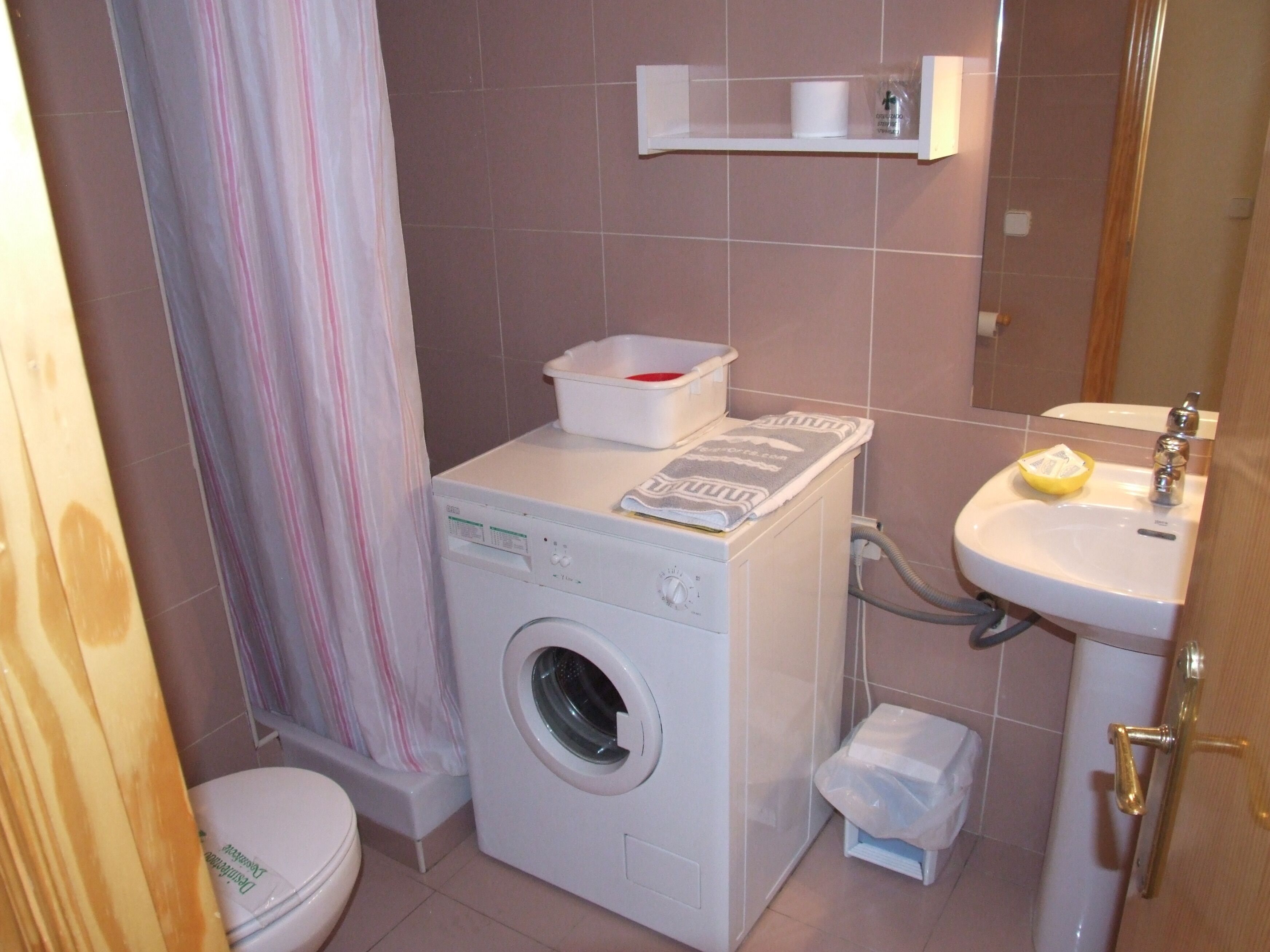 A compact bathroom with a washing machine, a sink, and a toilet.