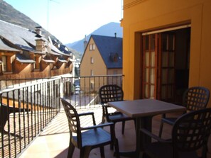Un balcón con mesa y sillas, con vistas a una montaña y una calle con edificios.