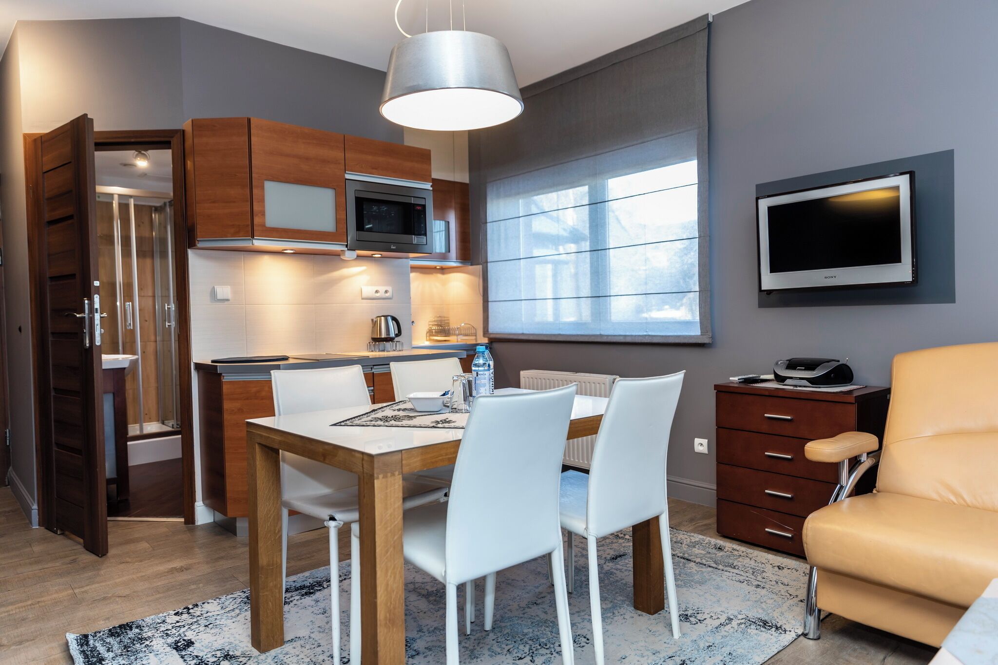 A modern kitchen with wooden cabinets, a built-in microwave, and a dining area with a table and chairs.