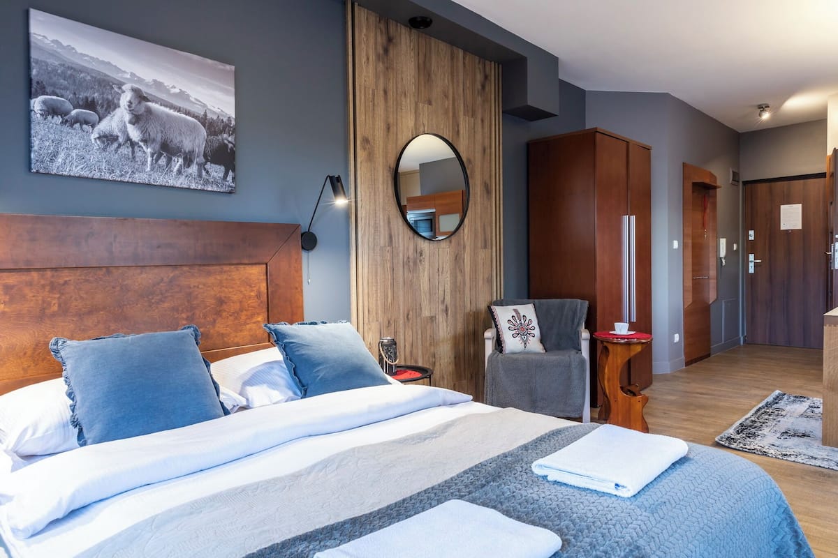 Una habitación de hotel moderna con una cama grande, un armario de madera, un espejo y un cuadro en la pared.