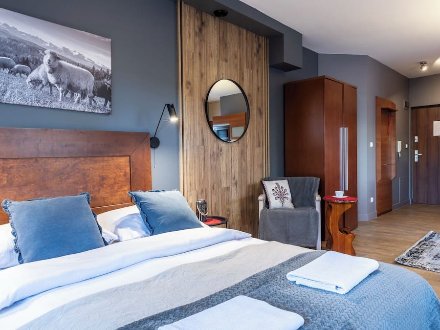 Una habitación de hotel moderna con una cama grande, un armario de madera, un espejo y un cuadro en la pared.