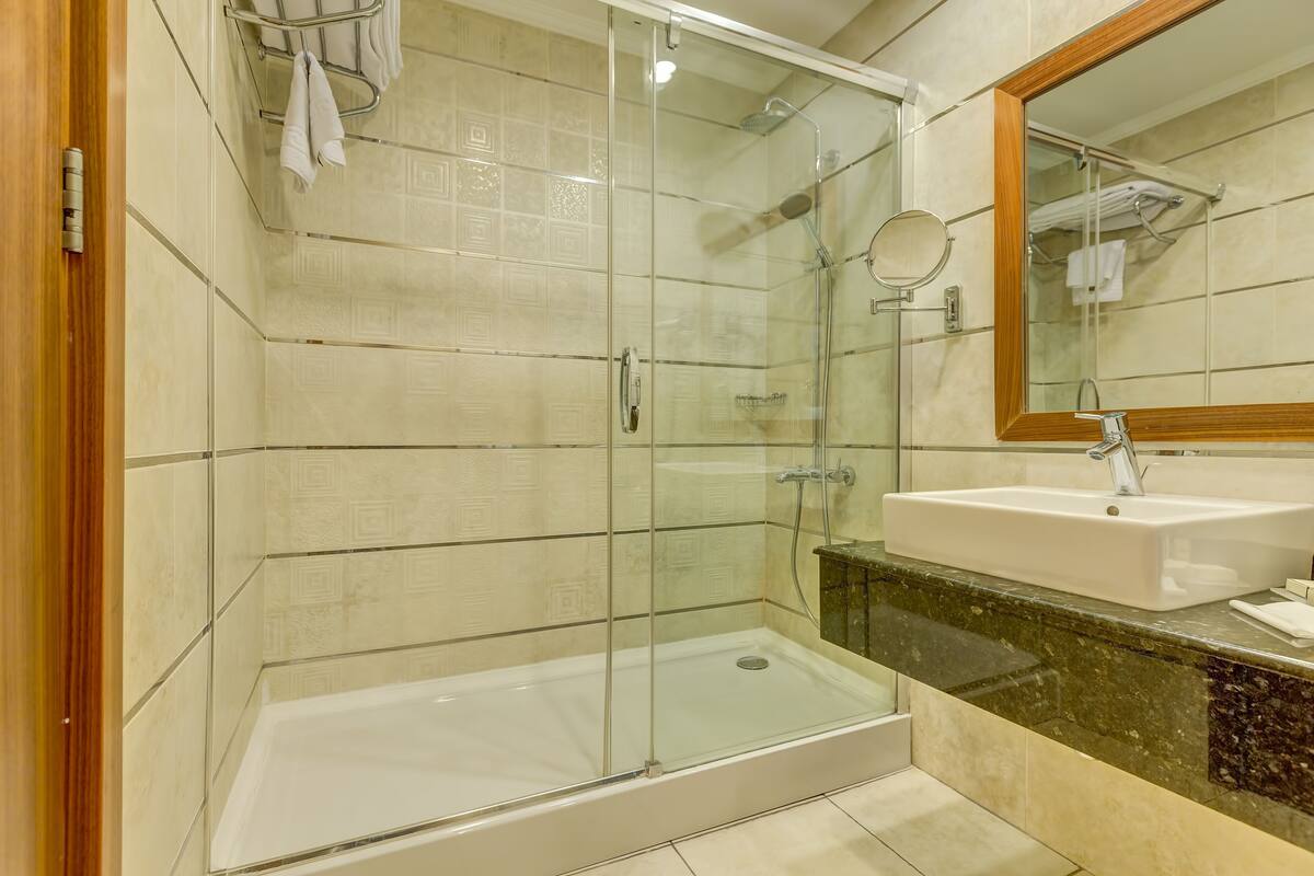 A bathroom with a glass-enclosed shower, a sink with a marble countertop, and a mirror.