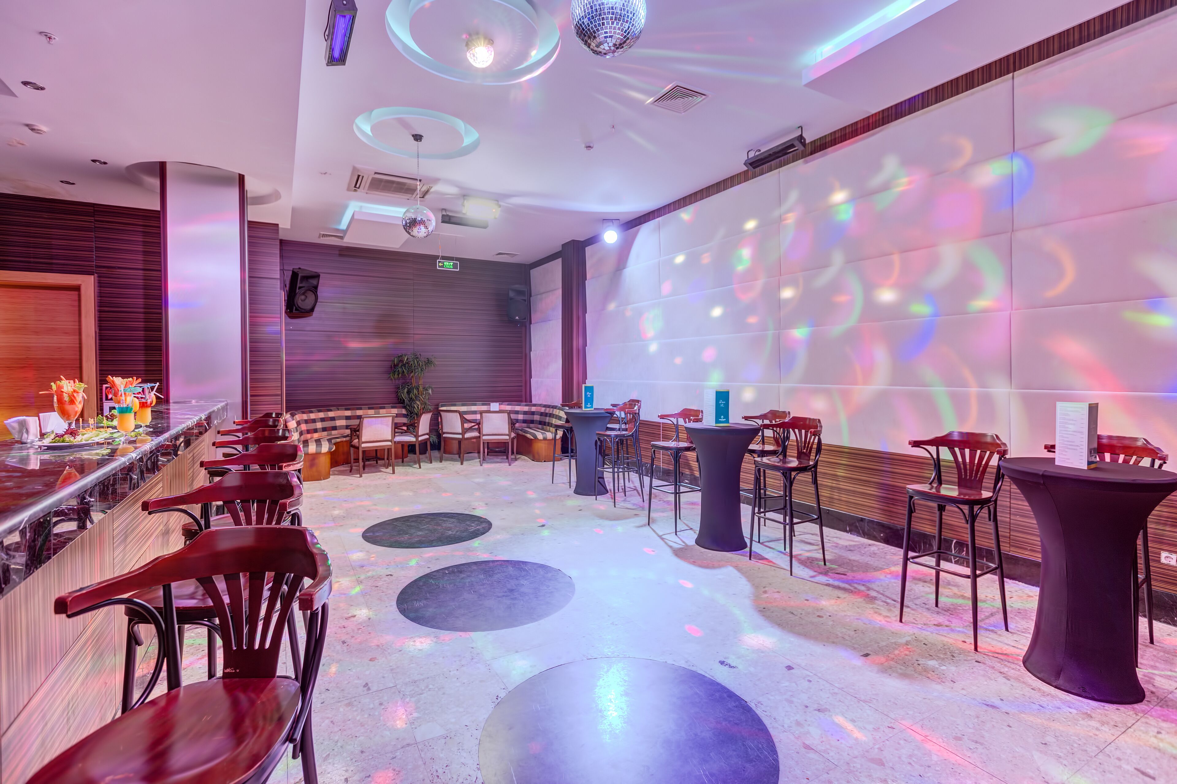 A modern bar area with a long counter, multiple seating options, and a disco ball.