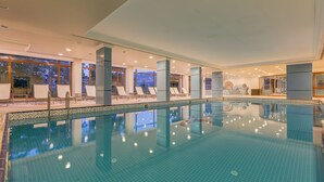 Una amplia piscina interior con agua cristalina, rodeada de sillones de descanso y un suelo de baldosas.