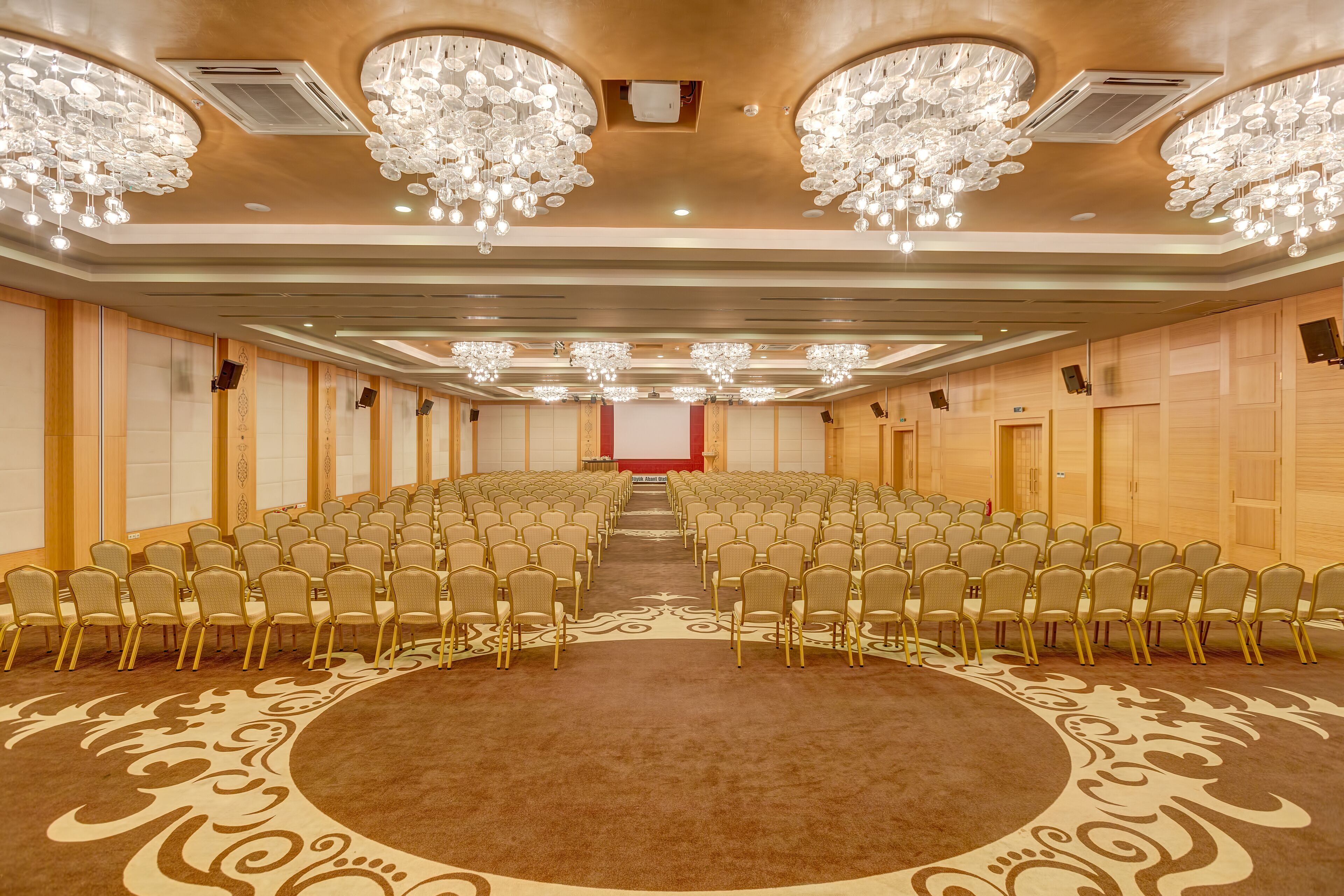 Un salón de conferencias con filas de sillas, una amplia zona alfombrada y candelabros.