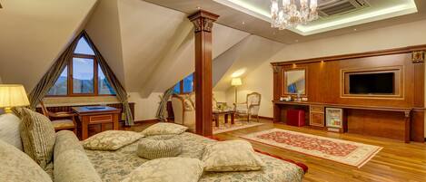 A spacious attic bedroom with a large bed, a TV, a chandelier, and a view of the sky through a window.