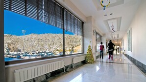 Un pasillo de hotel con grandes ventanales, un árbol de Navidad y vista a un estacionamiento.