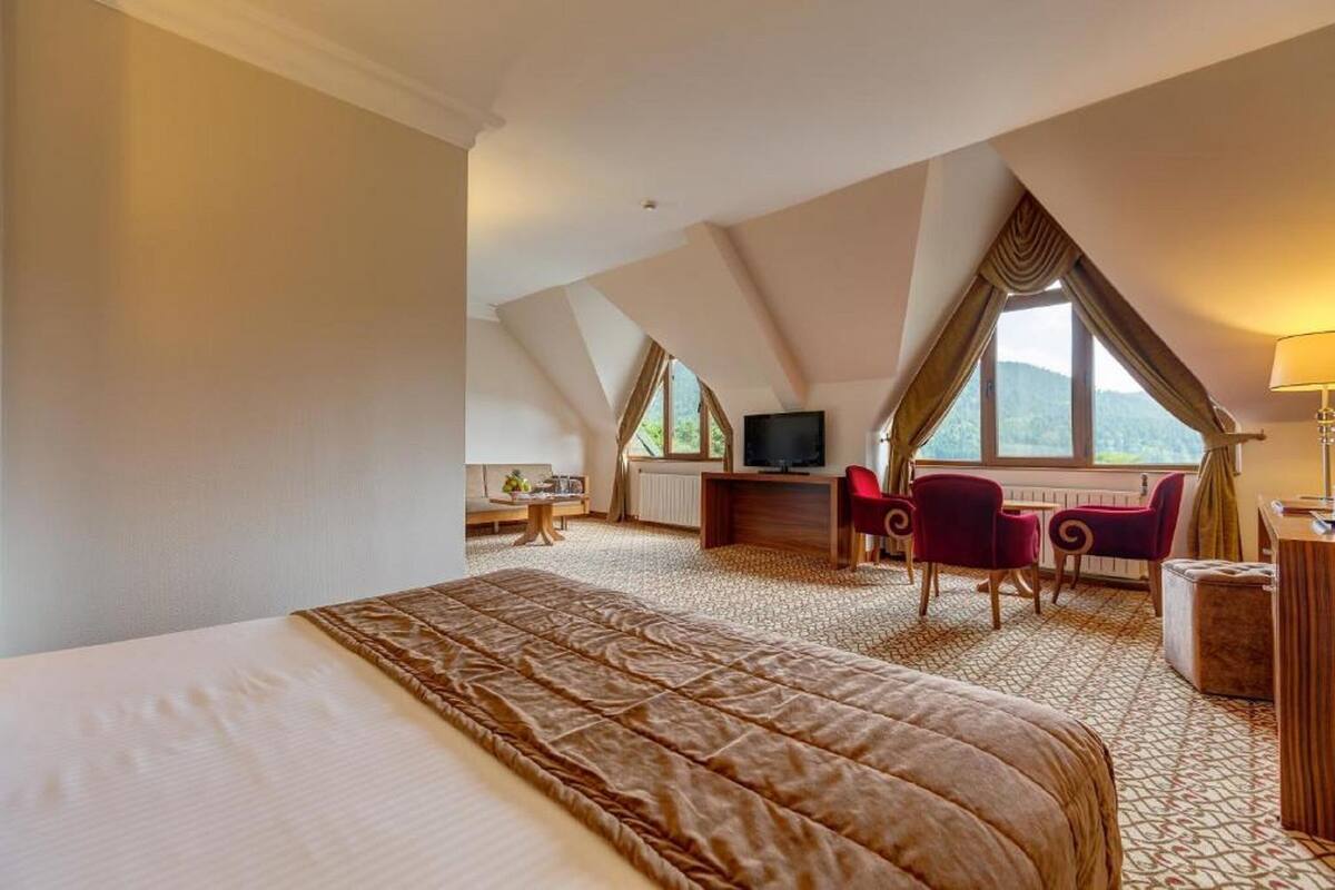 A hotel room with a large bed, a desk with a computer, a TV, and two chairs.