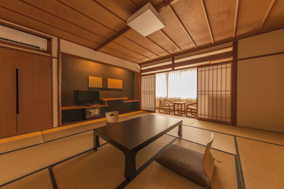 Ein traditioneller japanischer Raum mit Tatami-Bodenbelag, einem niedrigen Tisch, einem Fernseher und Schiebetüren.