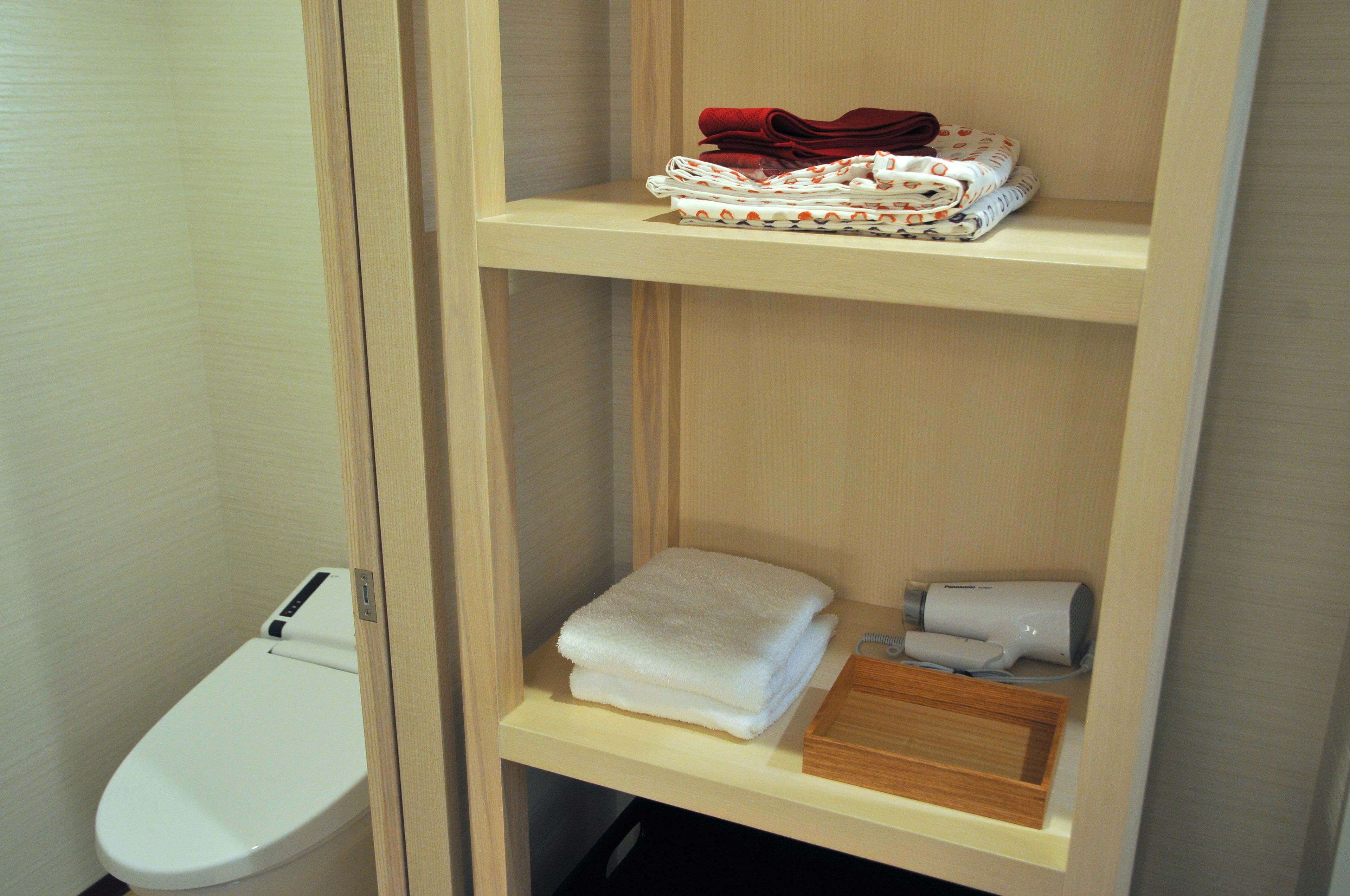 Un baño con inodoro, una repisa con toallas dobladas y un secador de pelo.