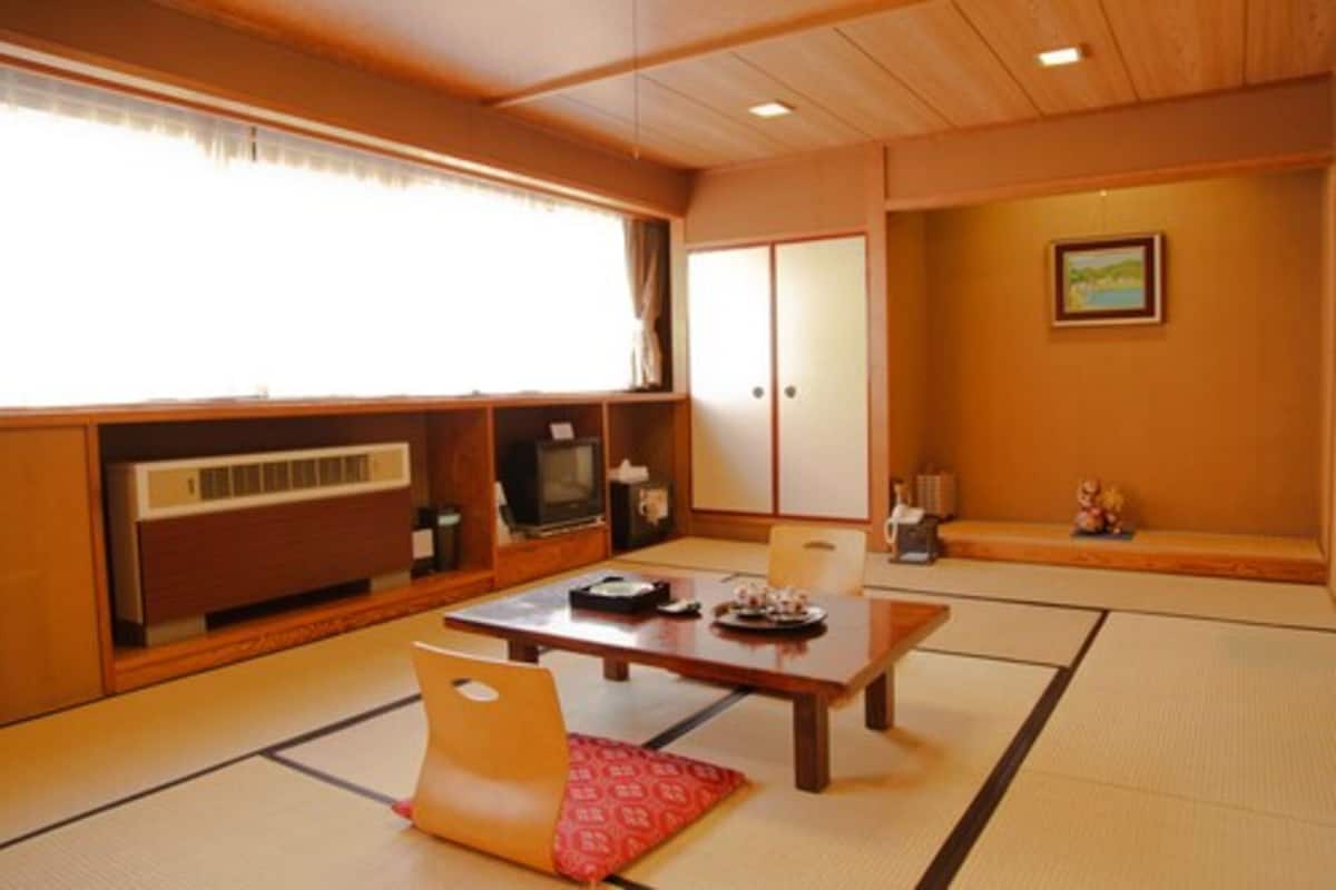 Ein traditioneller japanischer Raum mit Tatami-Boden, einem niedrigen Tisch und einem Fernseher.