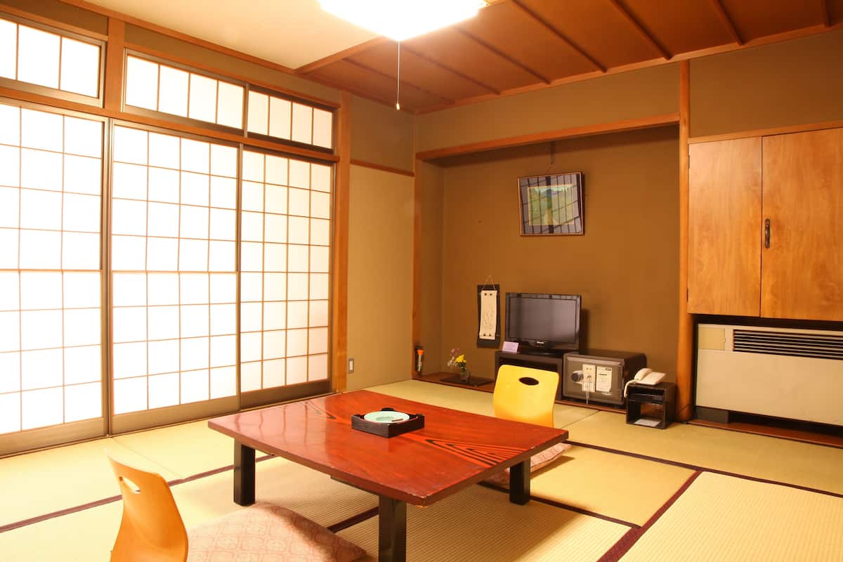 Ein traditioneller japanischer Raum mit Tatami-Böden, einem Holztisch, einem Fernseher und einem Schrank.