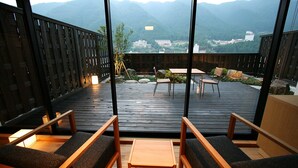 Um deck de madeira com assentos e mesa, com vista para montanhas e edifícios.