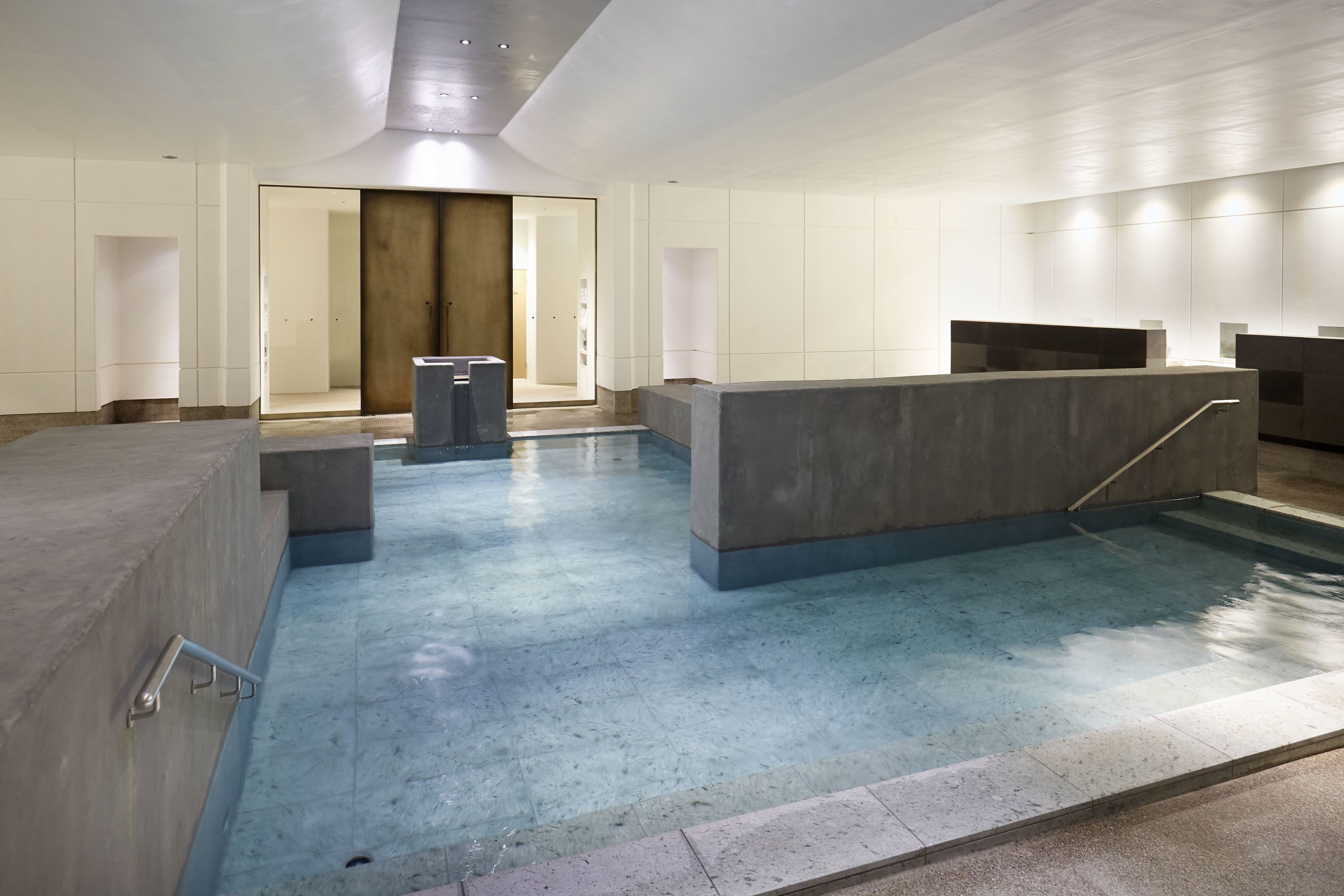 A modern indoor pool area with a concrete reception desk, a clear pathway, and a wooden door in the background.