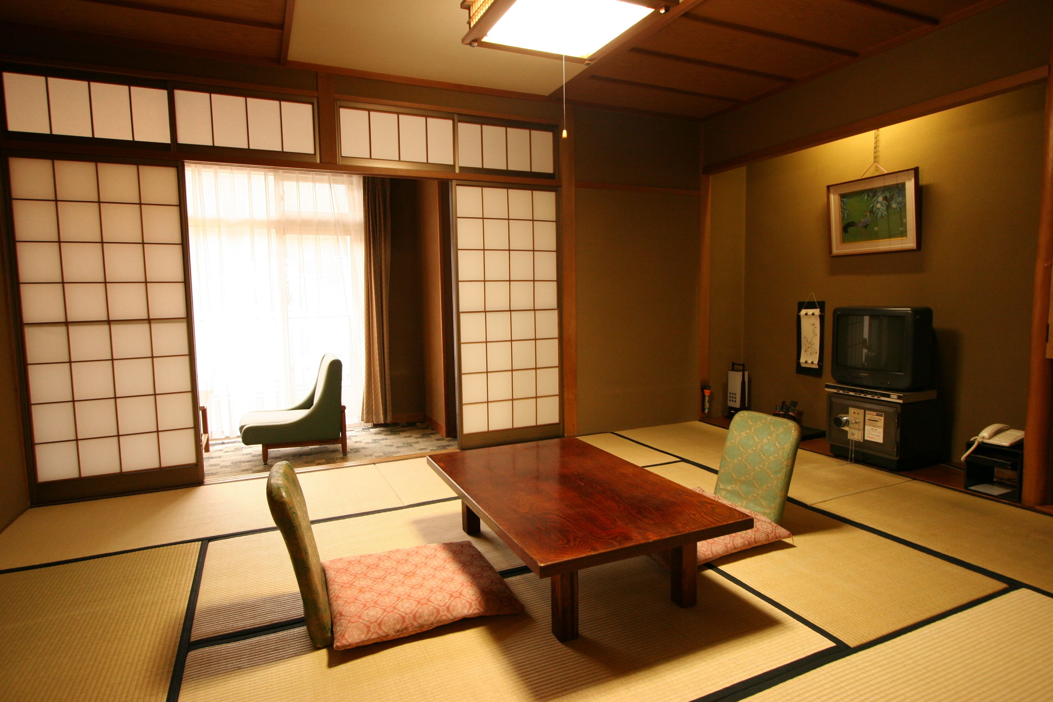 Una habitación japonesa tradicional con suelo de tatami, una mesa de madera, una silla verde, un televisor y una puerta corredera.