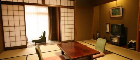 Una habitación japonesa tradicional con suelo de tatami, una mesa de madera, una silla verde, un televisor y una puerta corredera.
