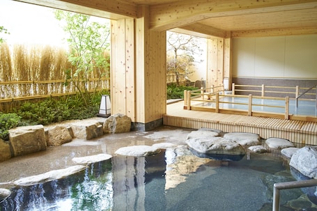 A traditional Japanese onsen with a wooden interior, stone bath, and a view of bamboo outside.