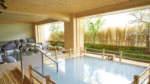 Uma onsen japonesa tradicional com grades de madeira, um banco de pedra e vista para bambu e árvores.