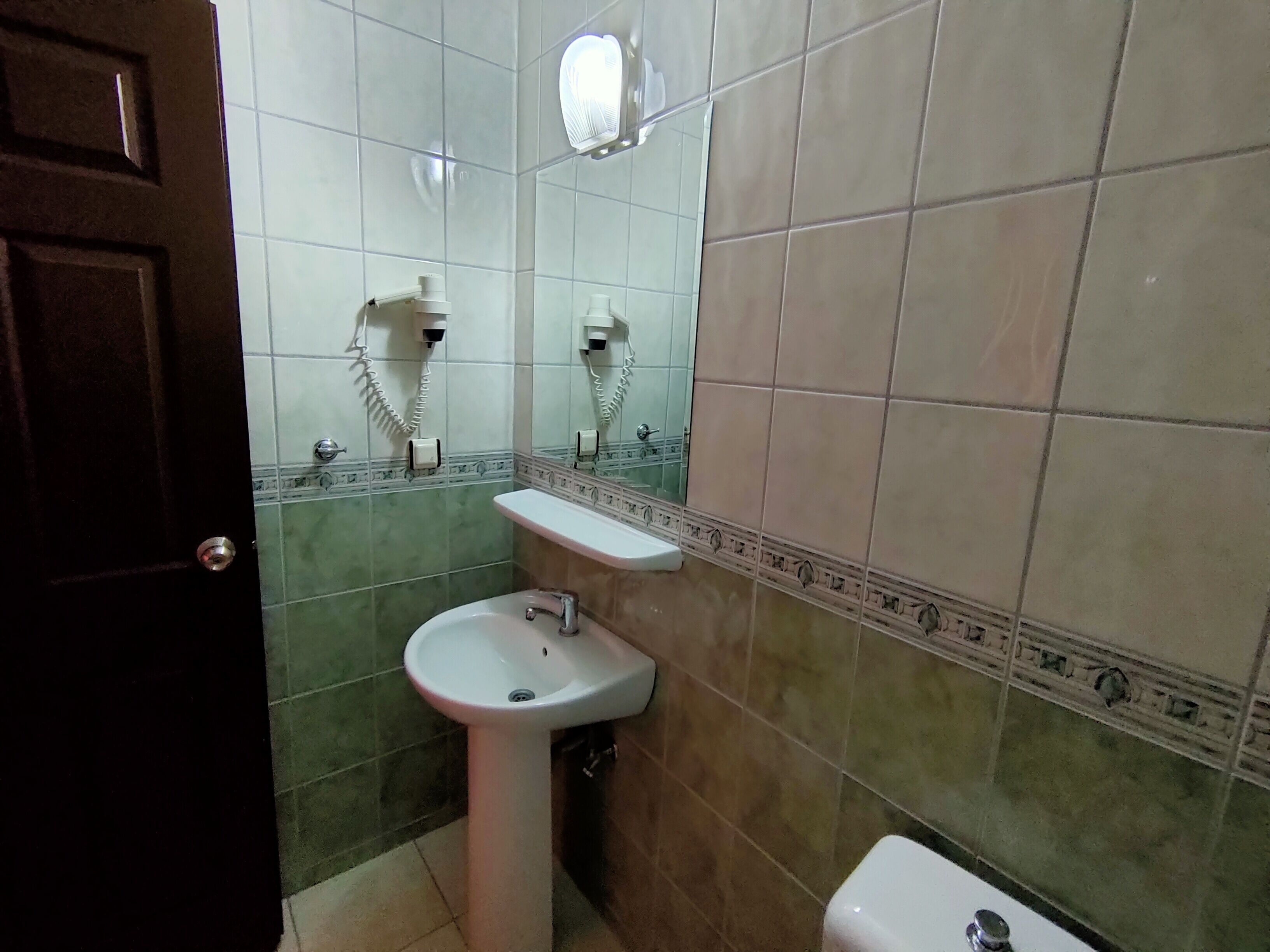 A bathroom with a sink, toilet, and two hair dryers mounted on the wall.
