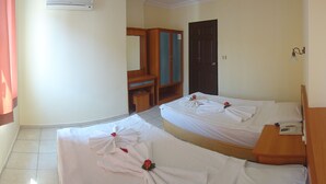 Habitación de hotel con dos camas, cada una con toallas dispuestas en forma de abanico y una rosa. Se observa un armario de madera, un escritorio y un teléfono a la derecha.