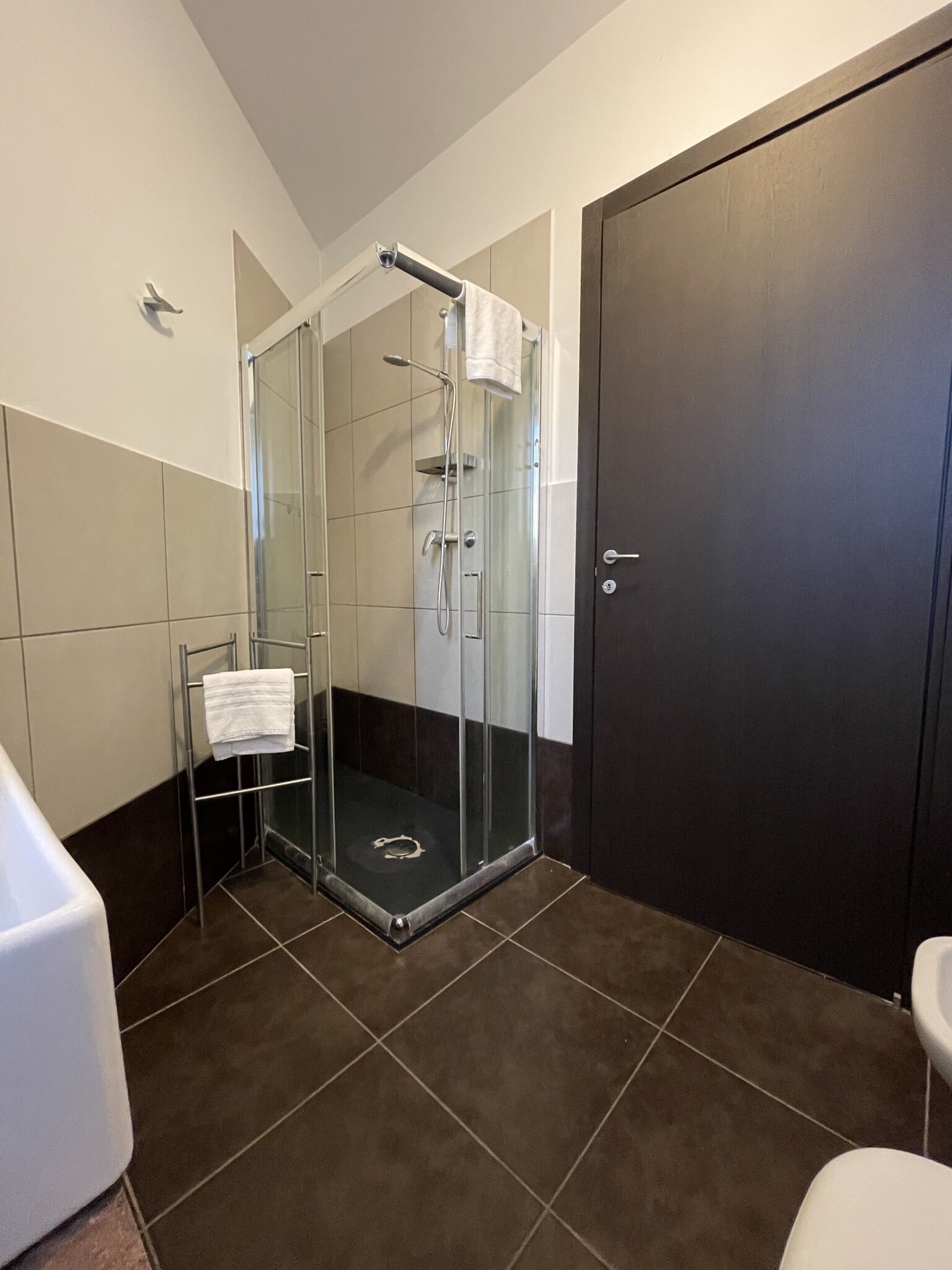 Un baño moderno con ducha de vidrio, una bañera blanca y una puerta oscura.