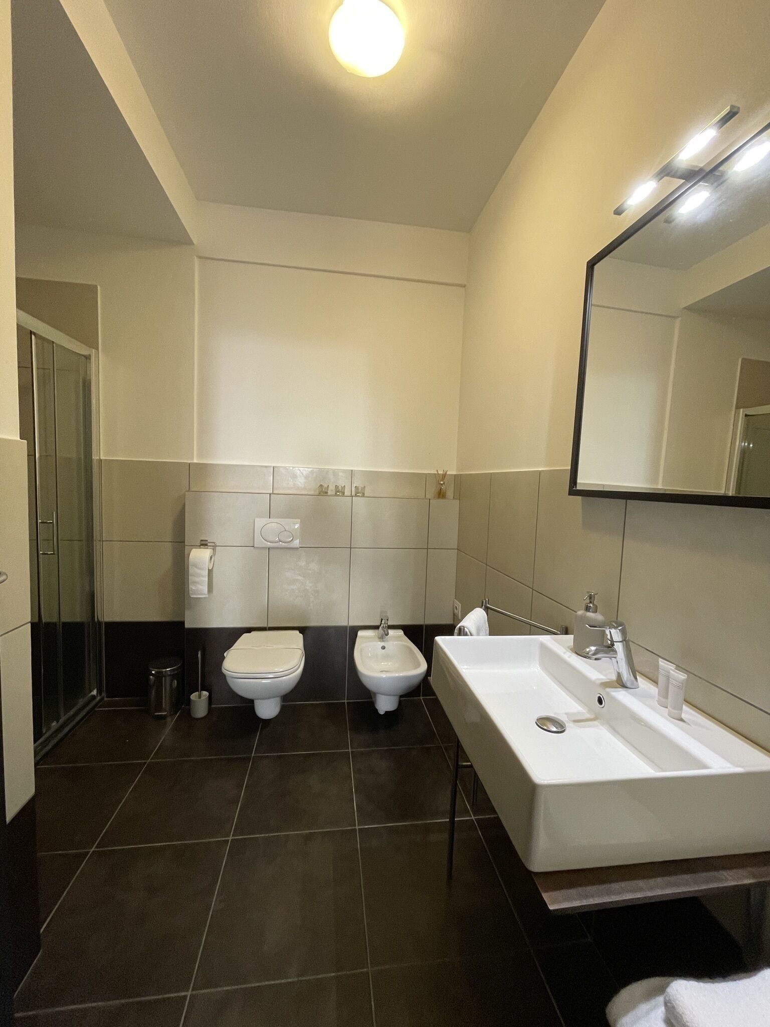 Un baño moderno con un lavamanos grande, dos inodoros y un bidé.