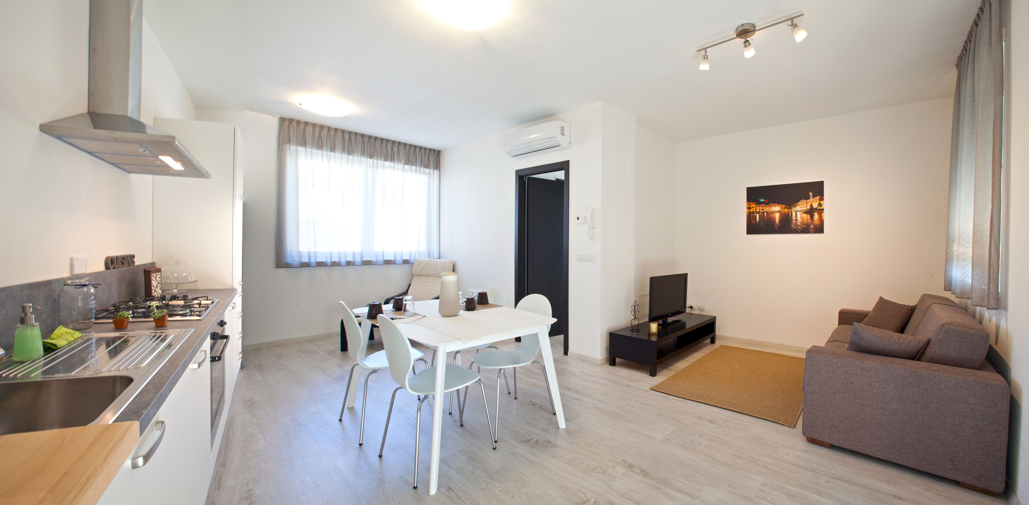 A modern kitchen with a dining area, a living room with a sofa, and a TV.