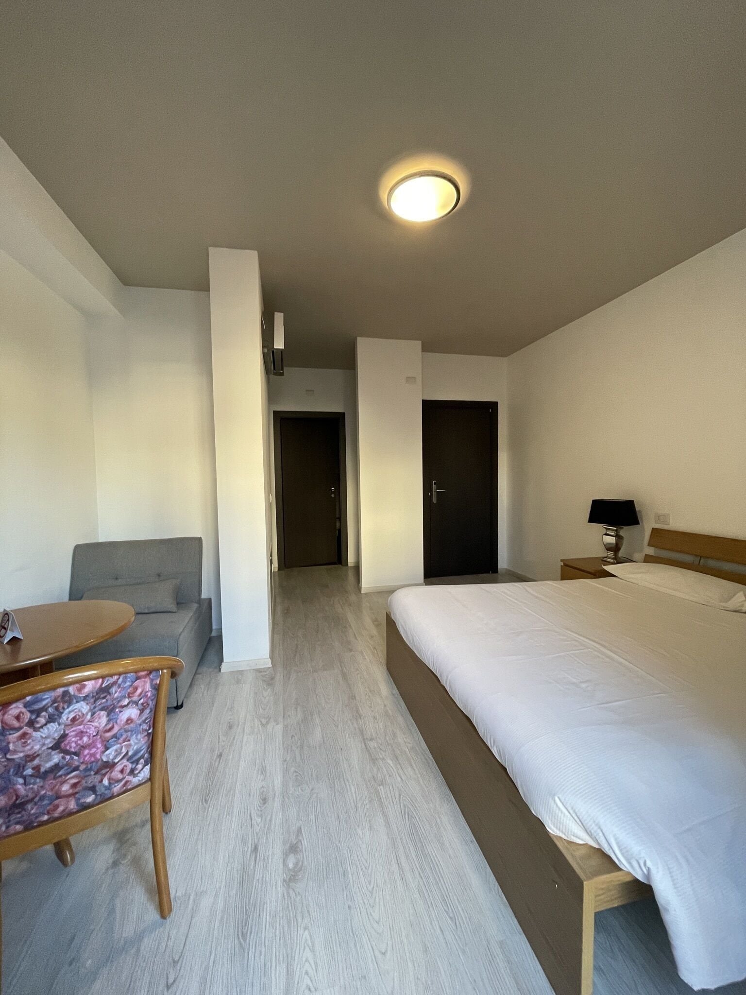 Et hotelværelse med en seng, et skrivebord med stol, en sofa og en dør til et andet rum.
