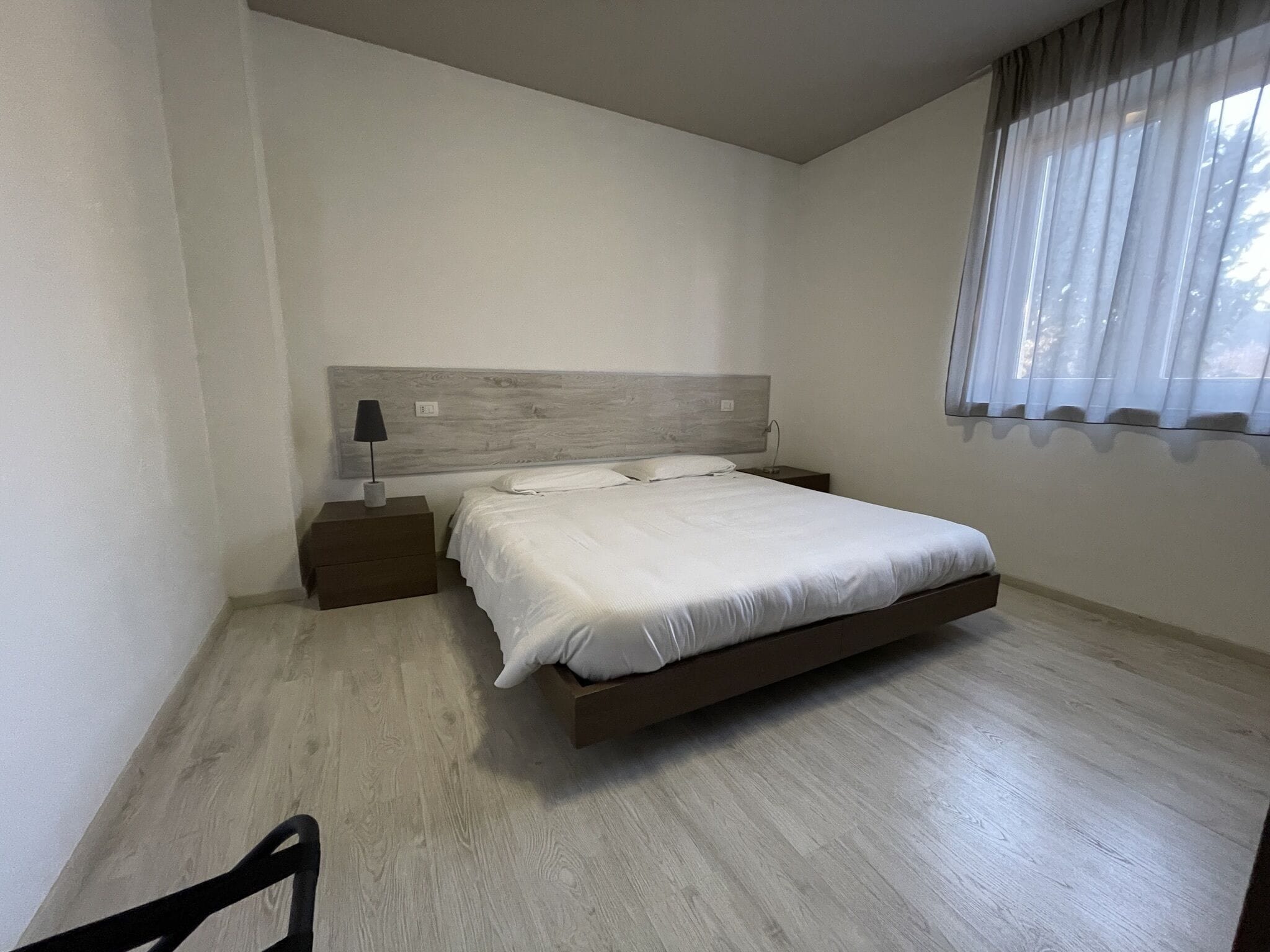 A bedroom with a bed, nightstand, lamp, and window with curtains.