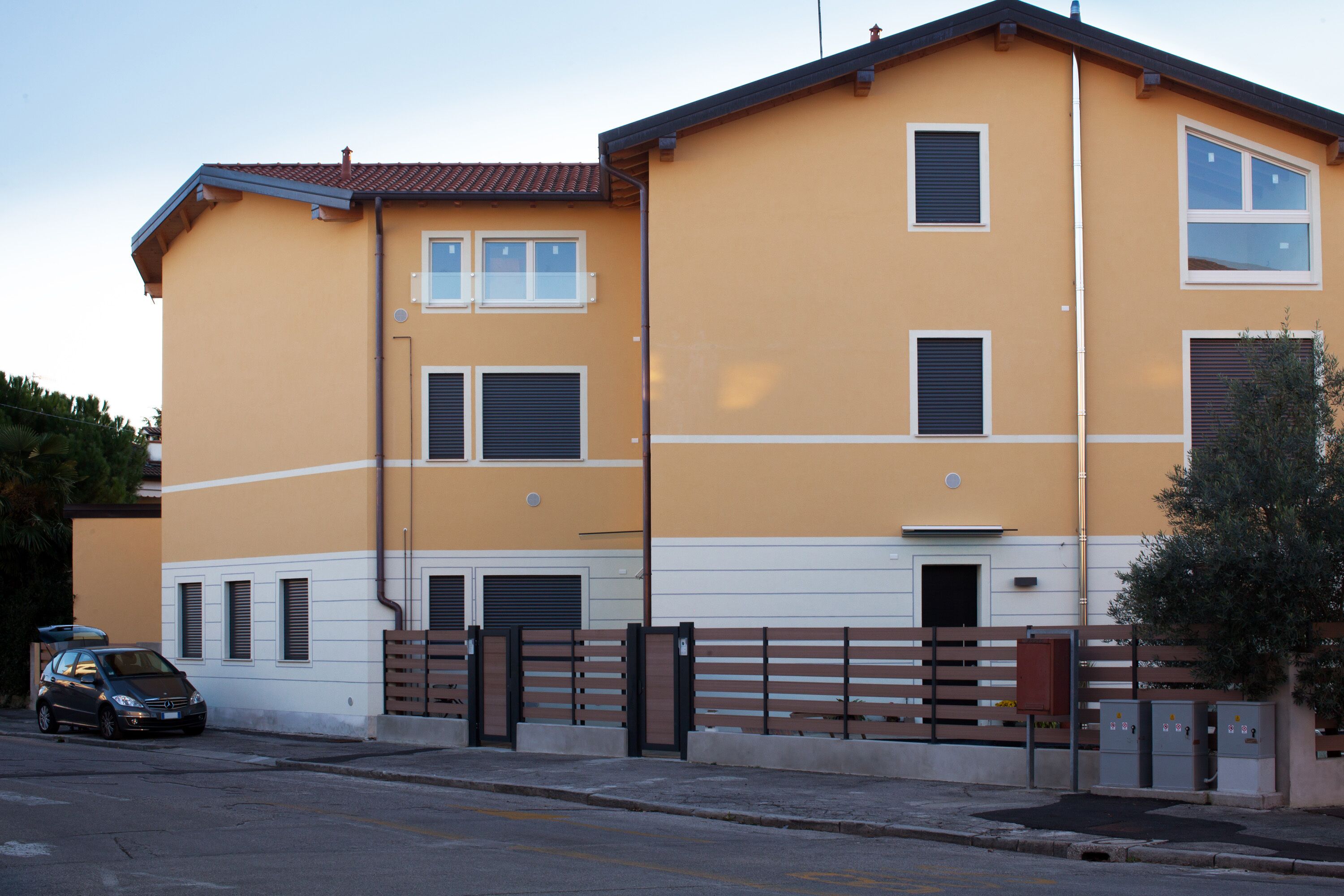 Un edificio de dos pisos con fachada amarilla, varias ventanas y una entrada protegida por una reja.