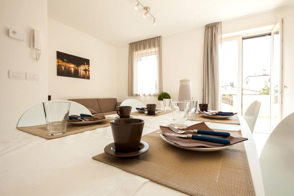 Un coin repas avec une table dressée pour deux personnes, comprenant des assiettes, des couverts et des verres.